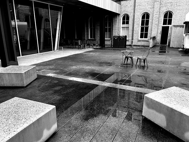 Puddles visible on plaza surface immediately adjacent to the new linear drain.