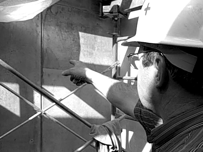 Contractor in hard hat points at mottled concrete wall surface.